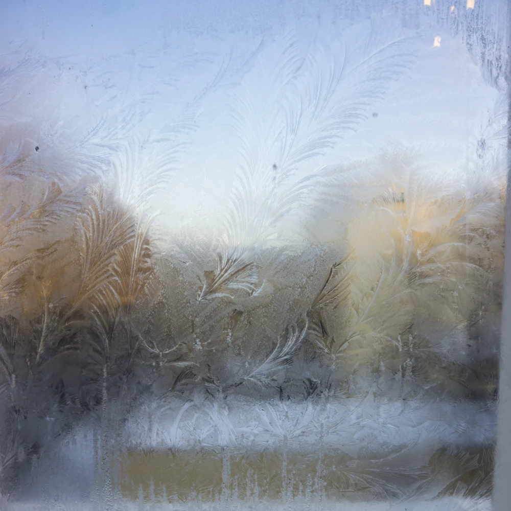 Fenêtre givrée vue de l’intérieur, montrant des motifs de cristaux de glace sur la vitre.