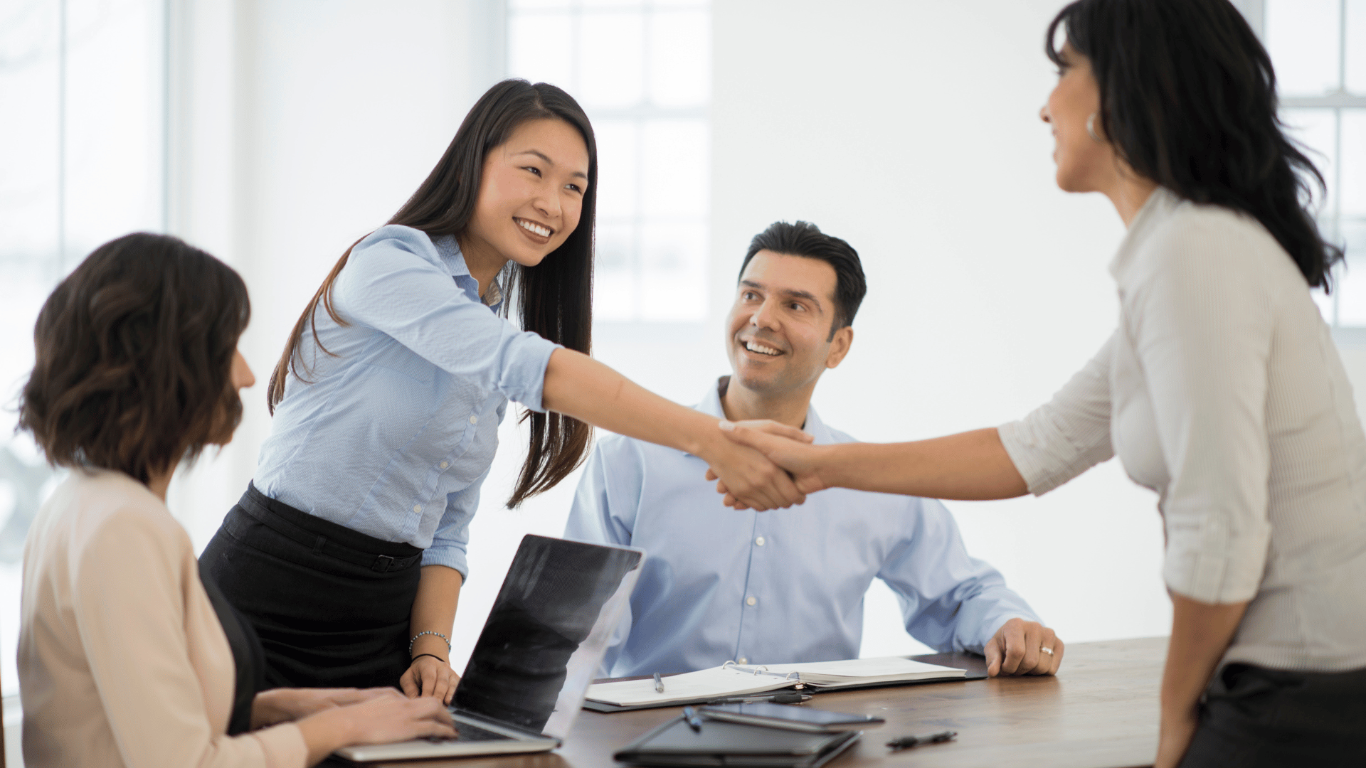 Four people at a meeting with two of them shaking hands