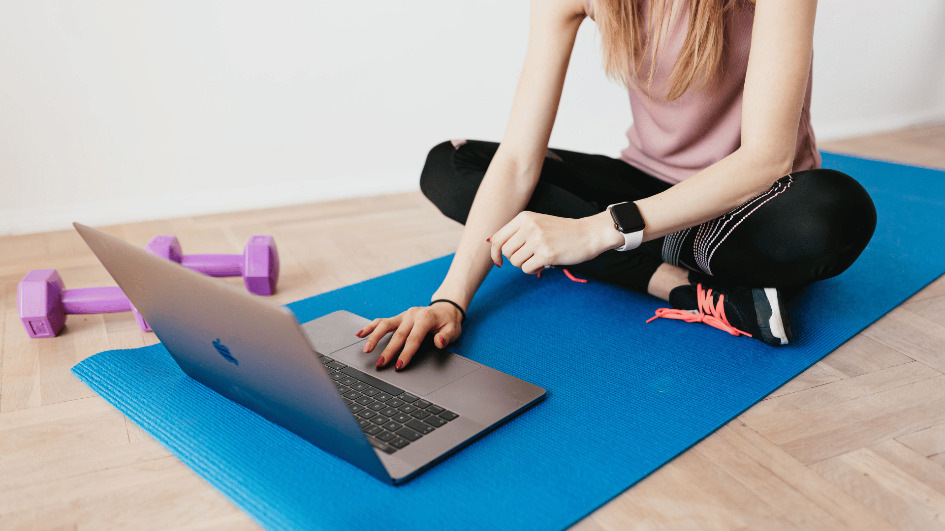 Woman taking an online fitness class on a yoga mat with a laptop