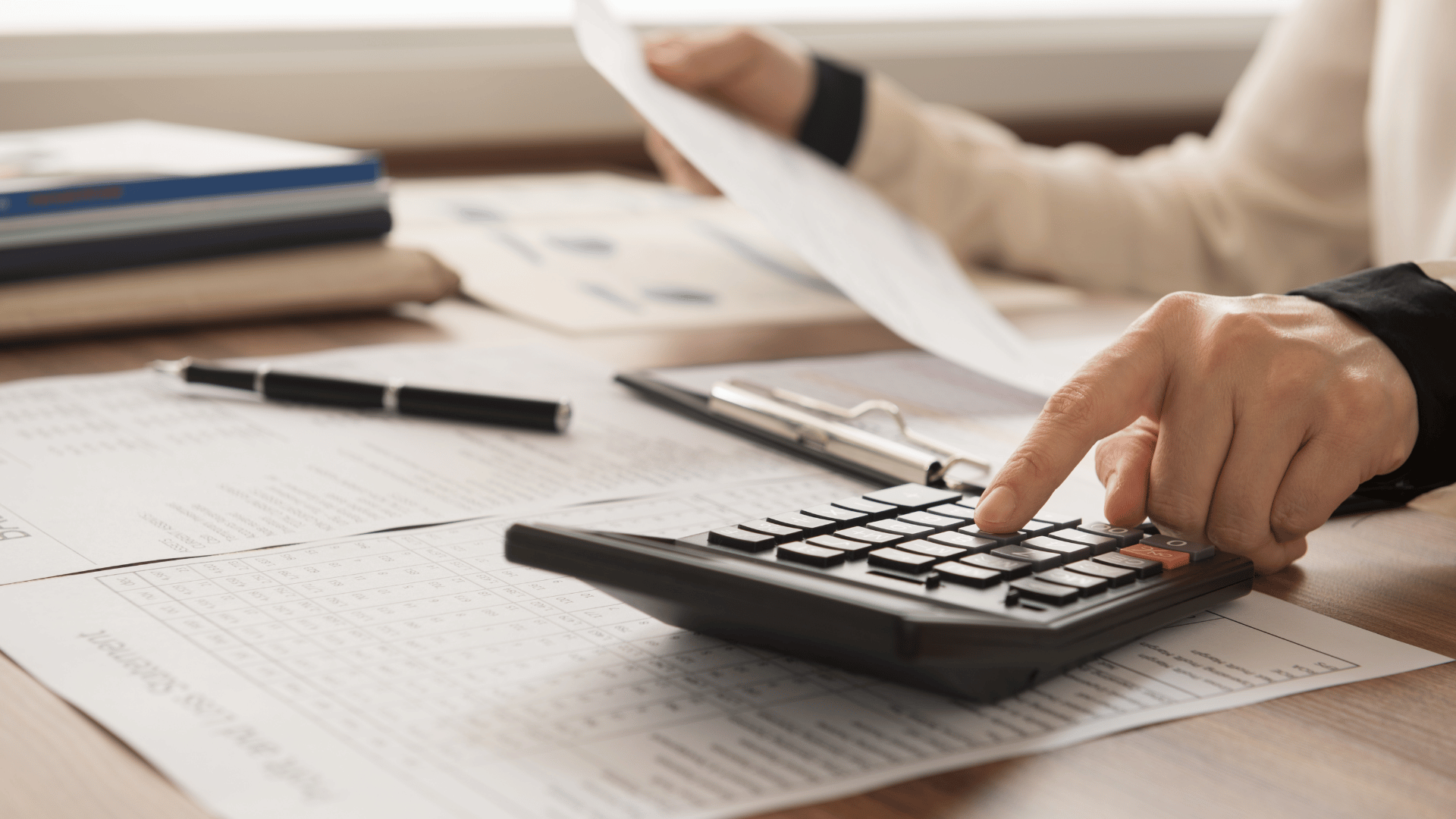 Person at a desk using a calculator and holding a sheet of paper