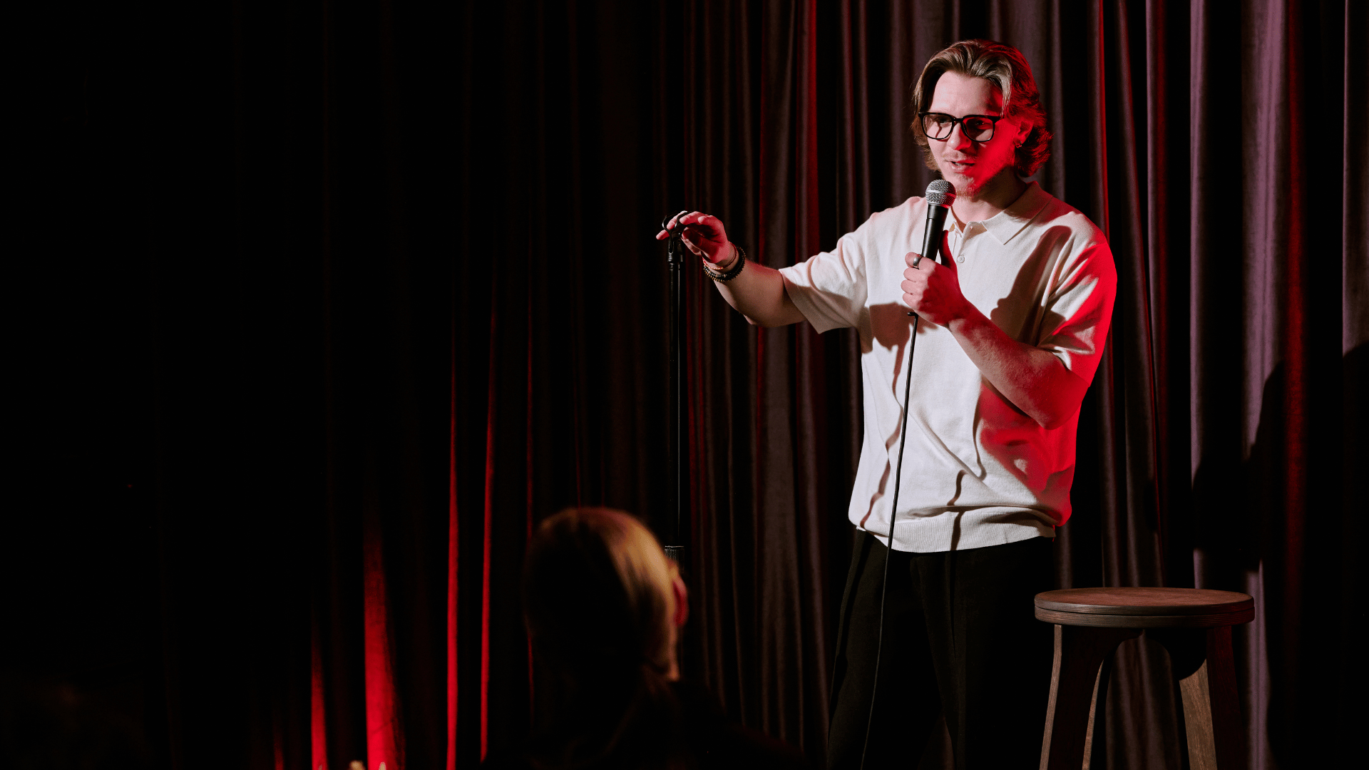 Man holding a mic at a comedy show with a curtain in the backgroun