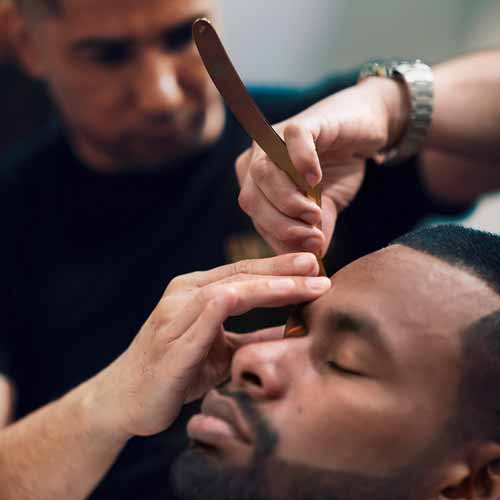 Man relaxes with eyes closed as barber shaves with a strait razor