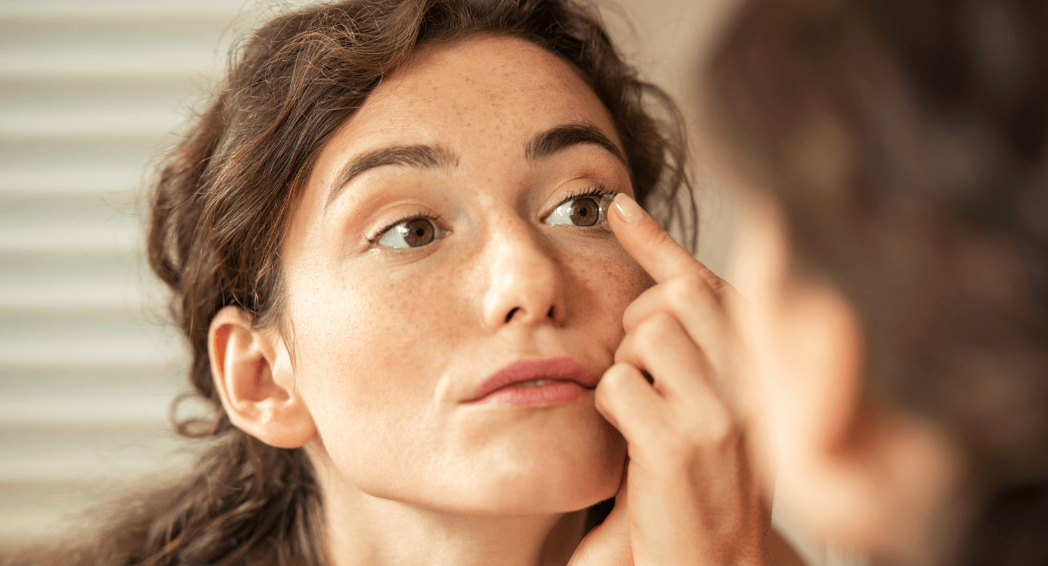 A brunette puts in a contact lens by looking in a mirror