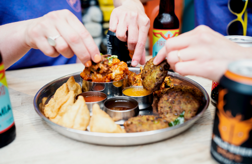 The hands of two people sharing a platter of Indian street food.