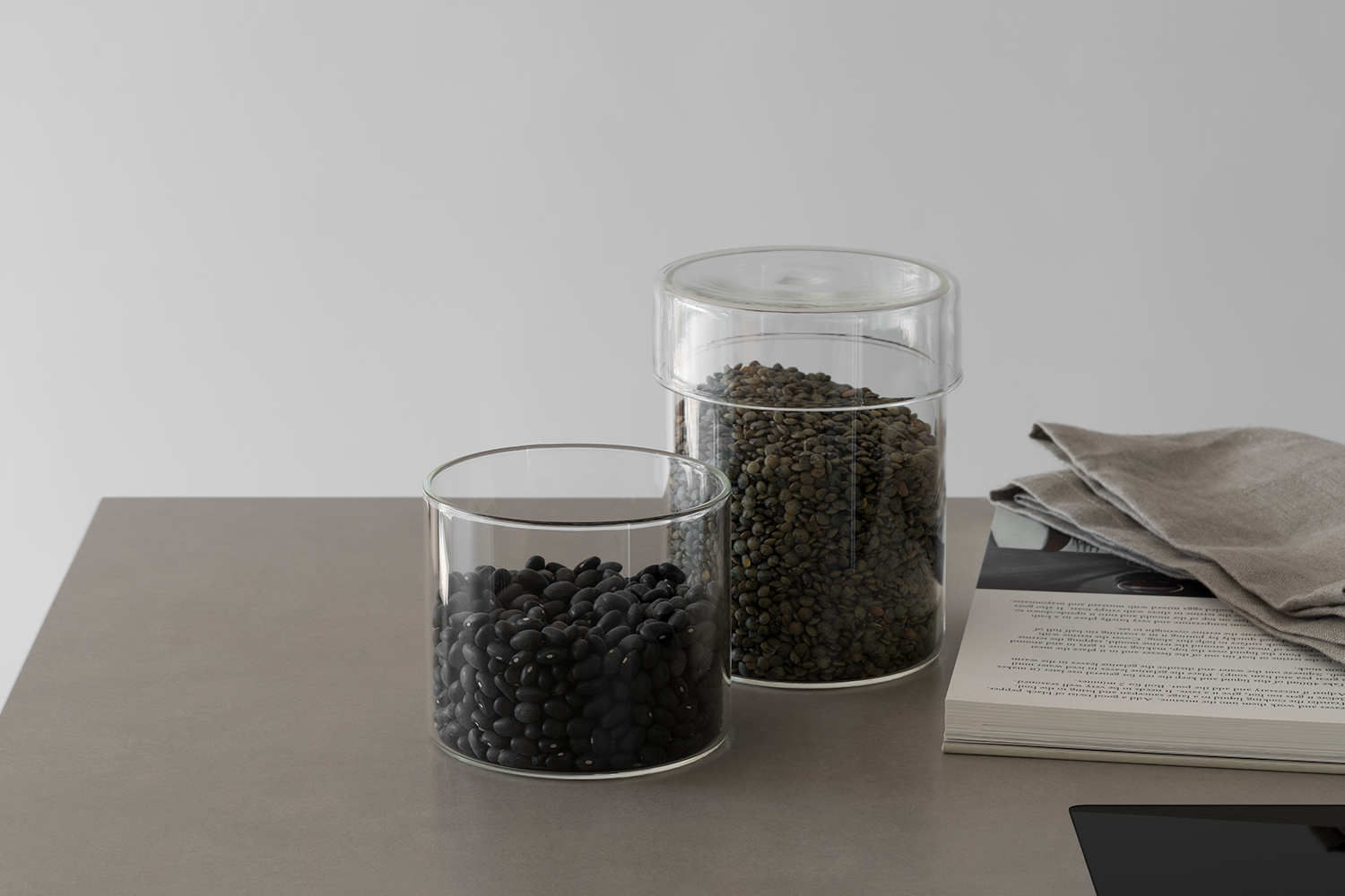 Minimal modern glass storage jars with lentils on a sintered stone work surface with recipe book and linen napkin