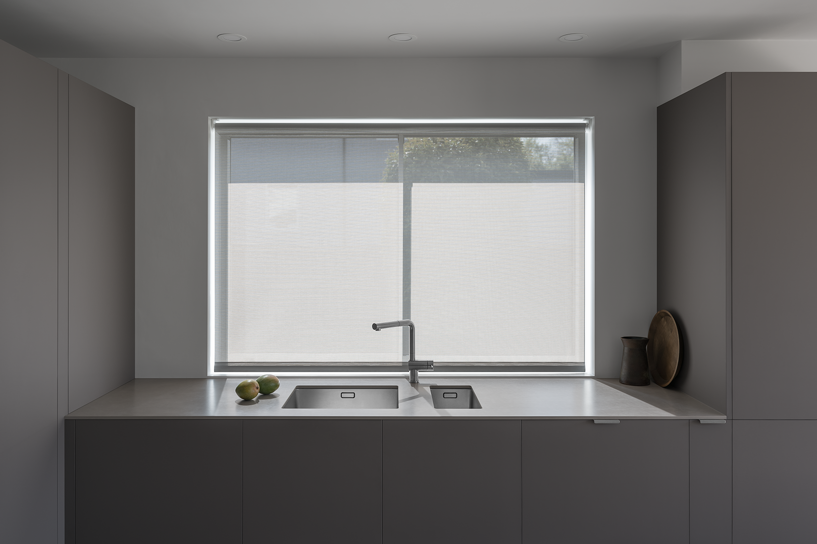 Japanese, minimal kitchen with white walls, light grey blind, grey brown cabinets, sintered stone worktop, stainless steel tap, wooden tray and mangos