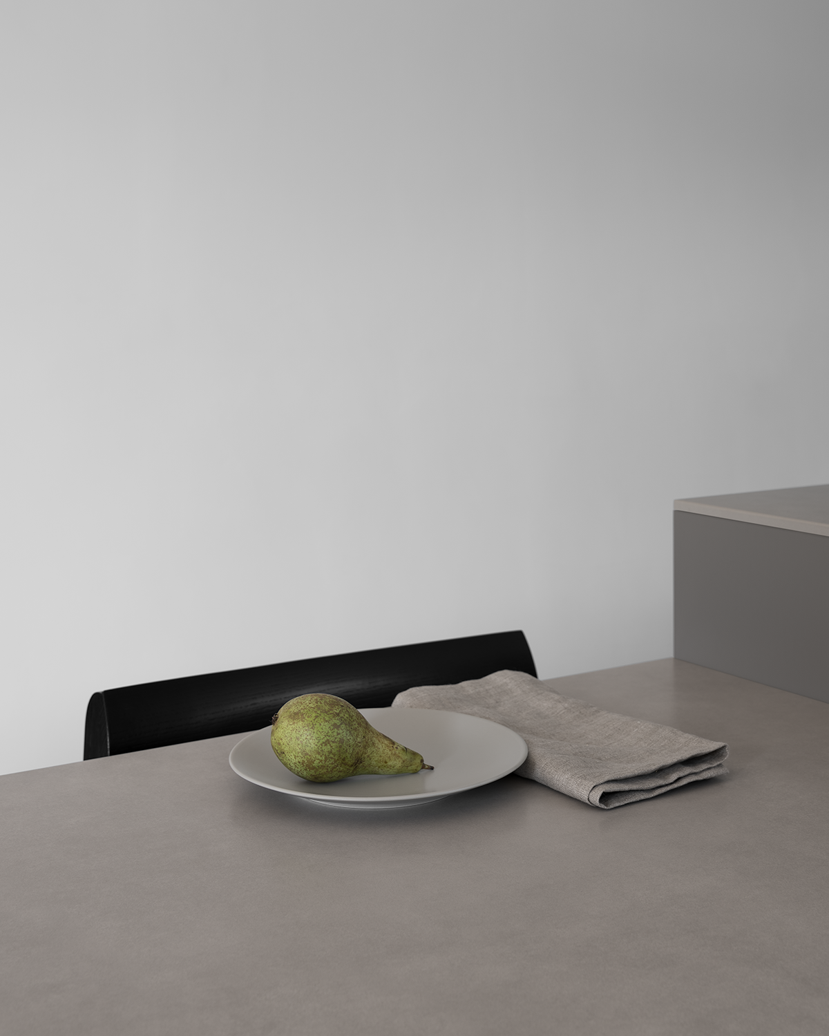 Custom modern sintered stone dining table in light grey, black modern Scandinavian dining chair, pear on a plate, linen napkin