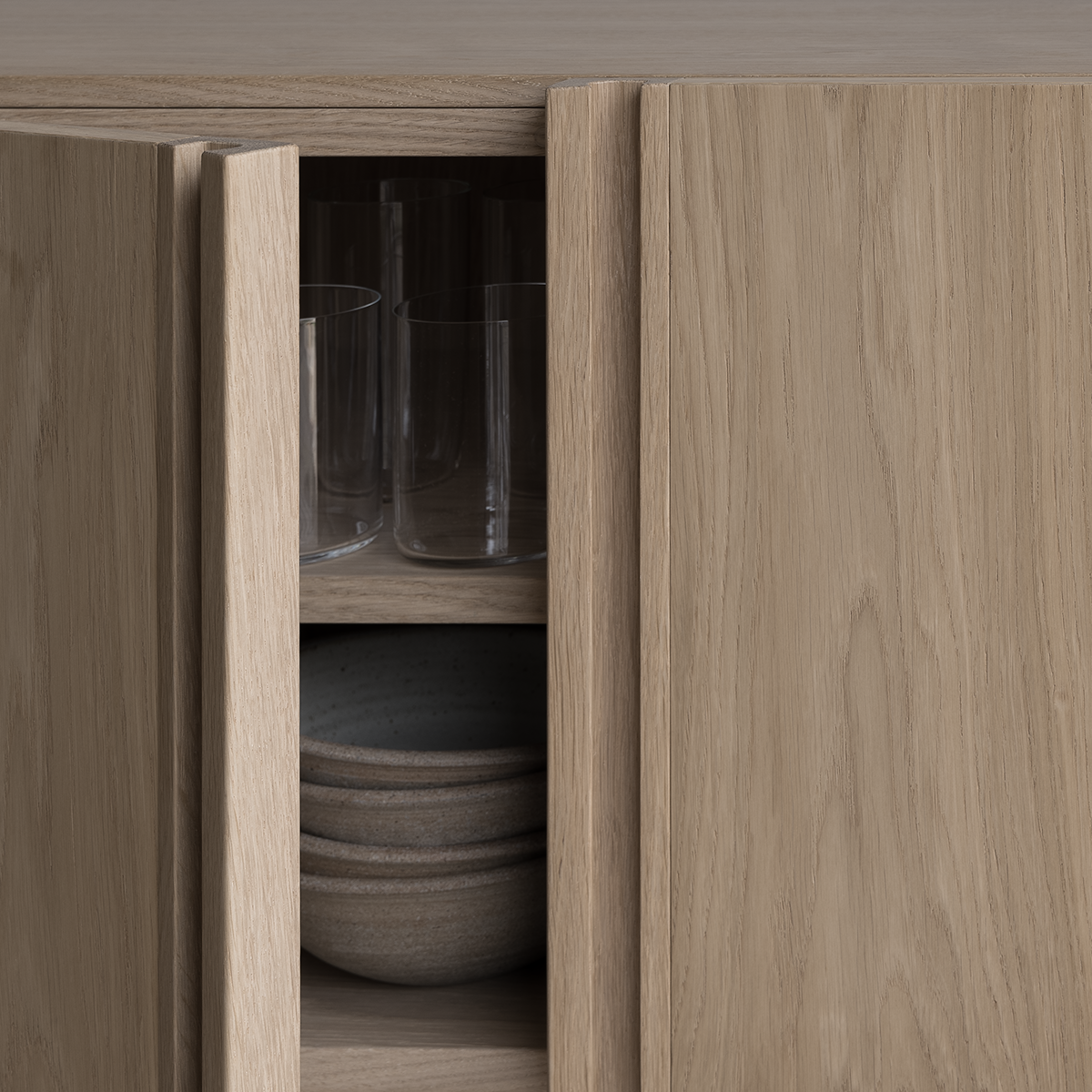 Bleached oak modern Scandinavian sideboard with open door showing glassware and bowls