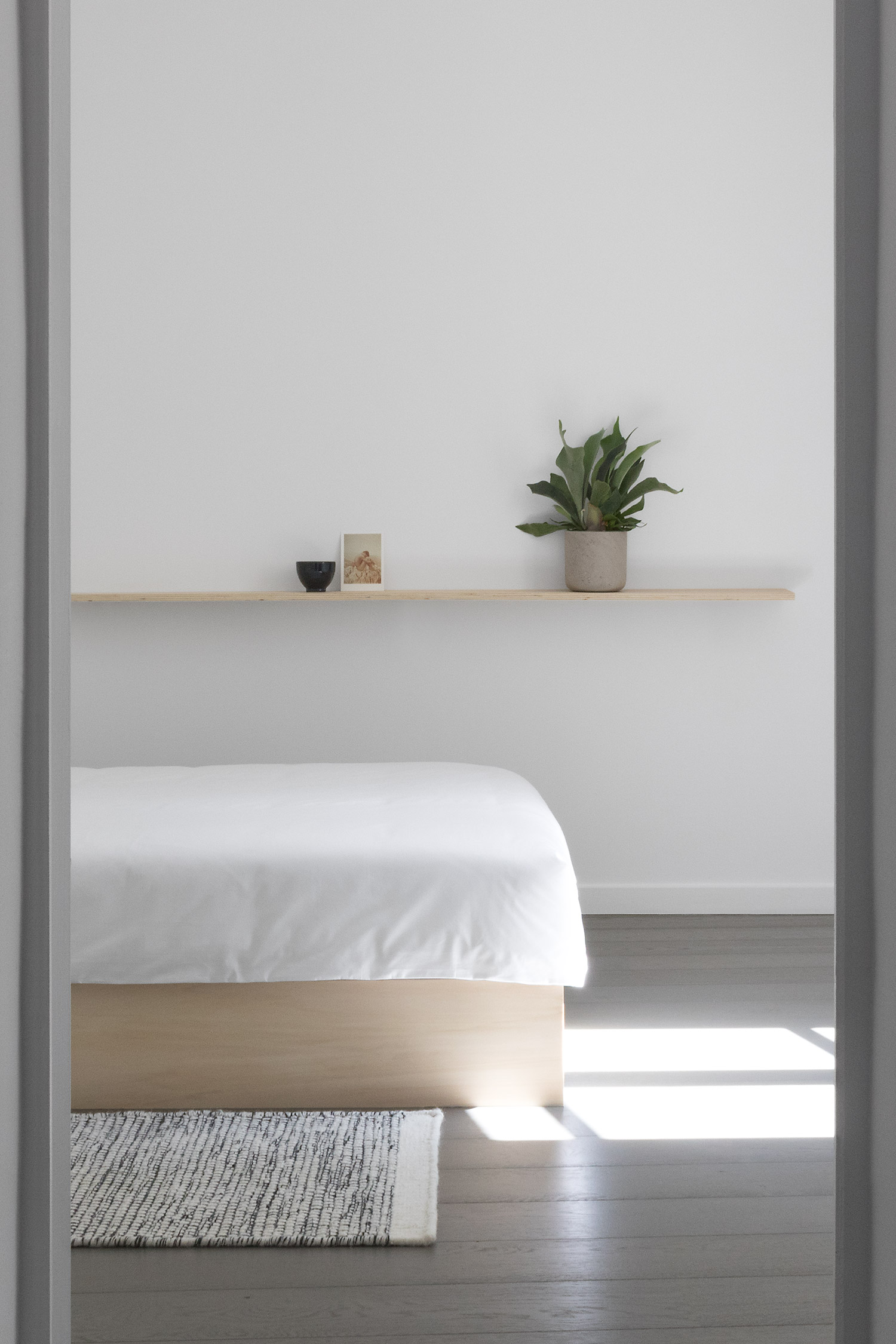 Doorway into minimal, modern Japanese style white bedroom with plywood bed
