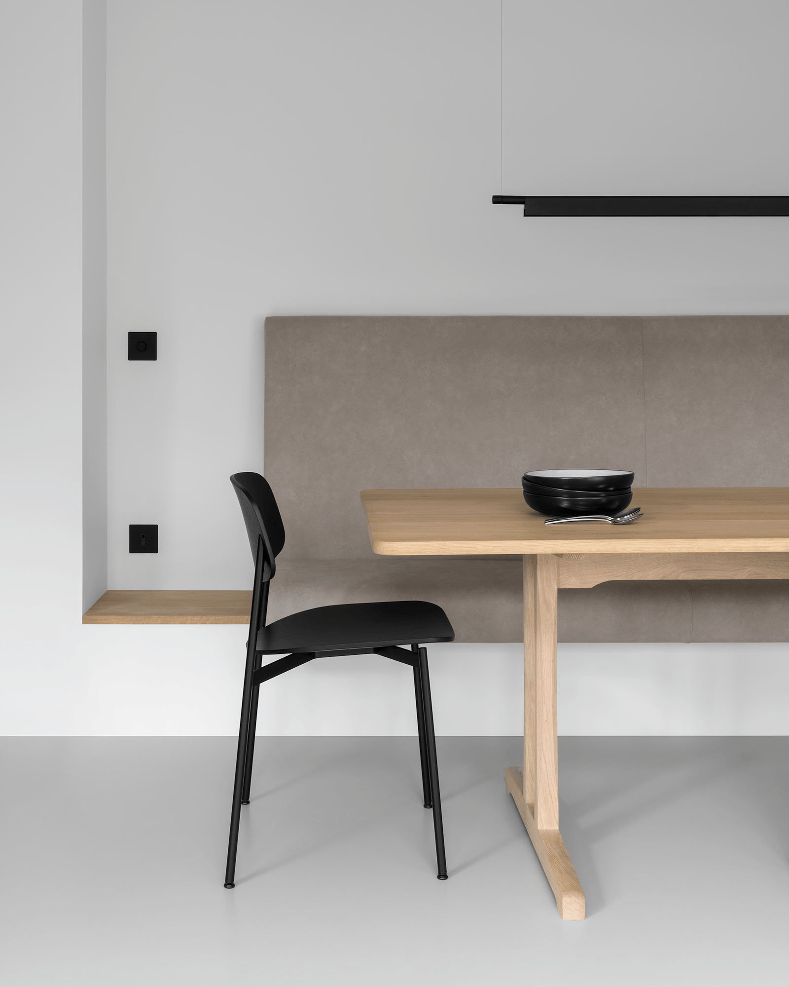 Japanese style minimal modern dining room with suede built in seating, Danish oak dining table, black Scandinavian dining chairs, modern black slimline pendant light, black bowls and stainless steel cutlery