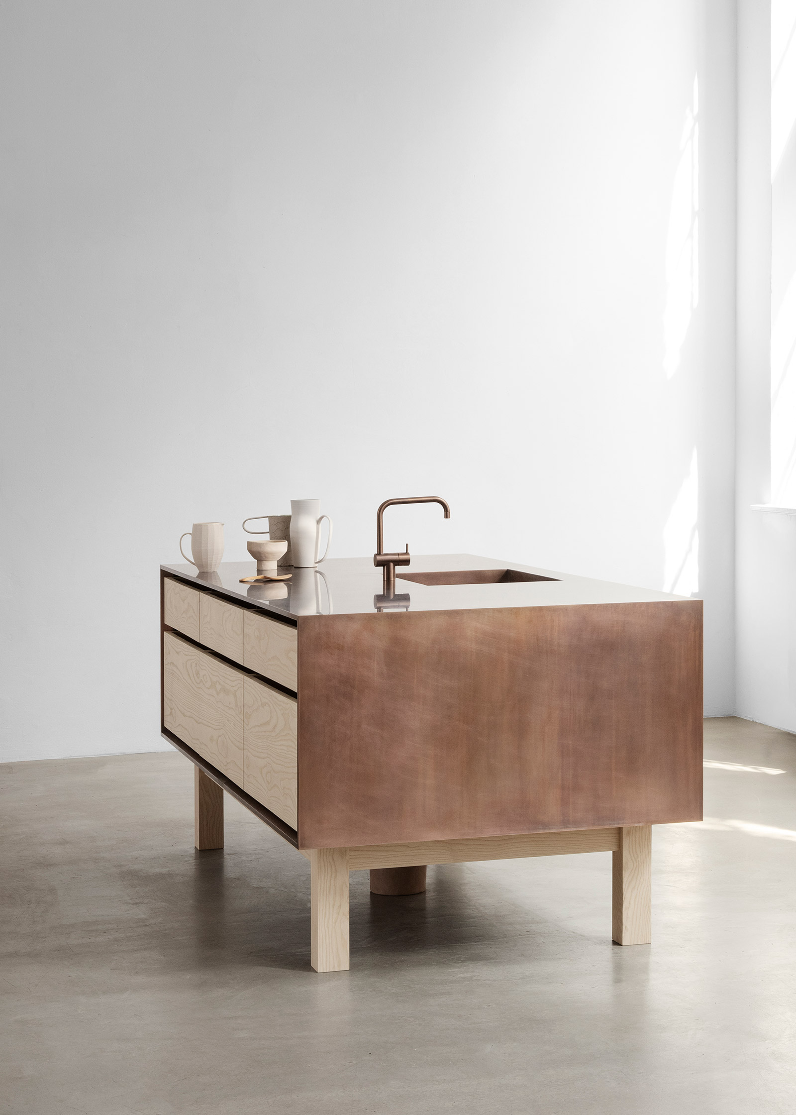 Minimal kitchen island made of ash and copper on concrete floor in white room