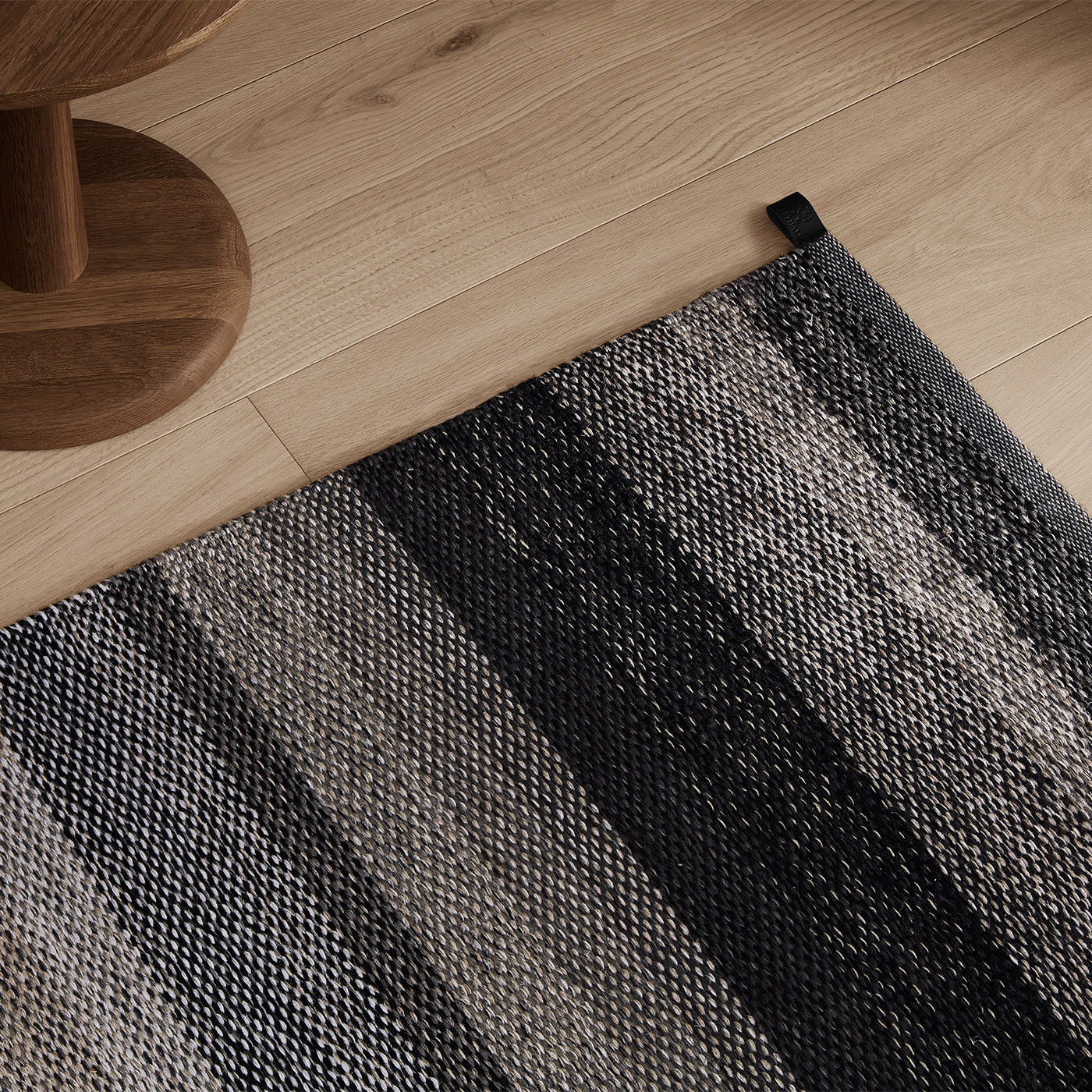 black and grey flat woven rug with light oak floor and modern smoked oak side table
