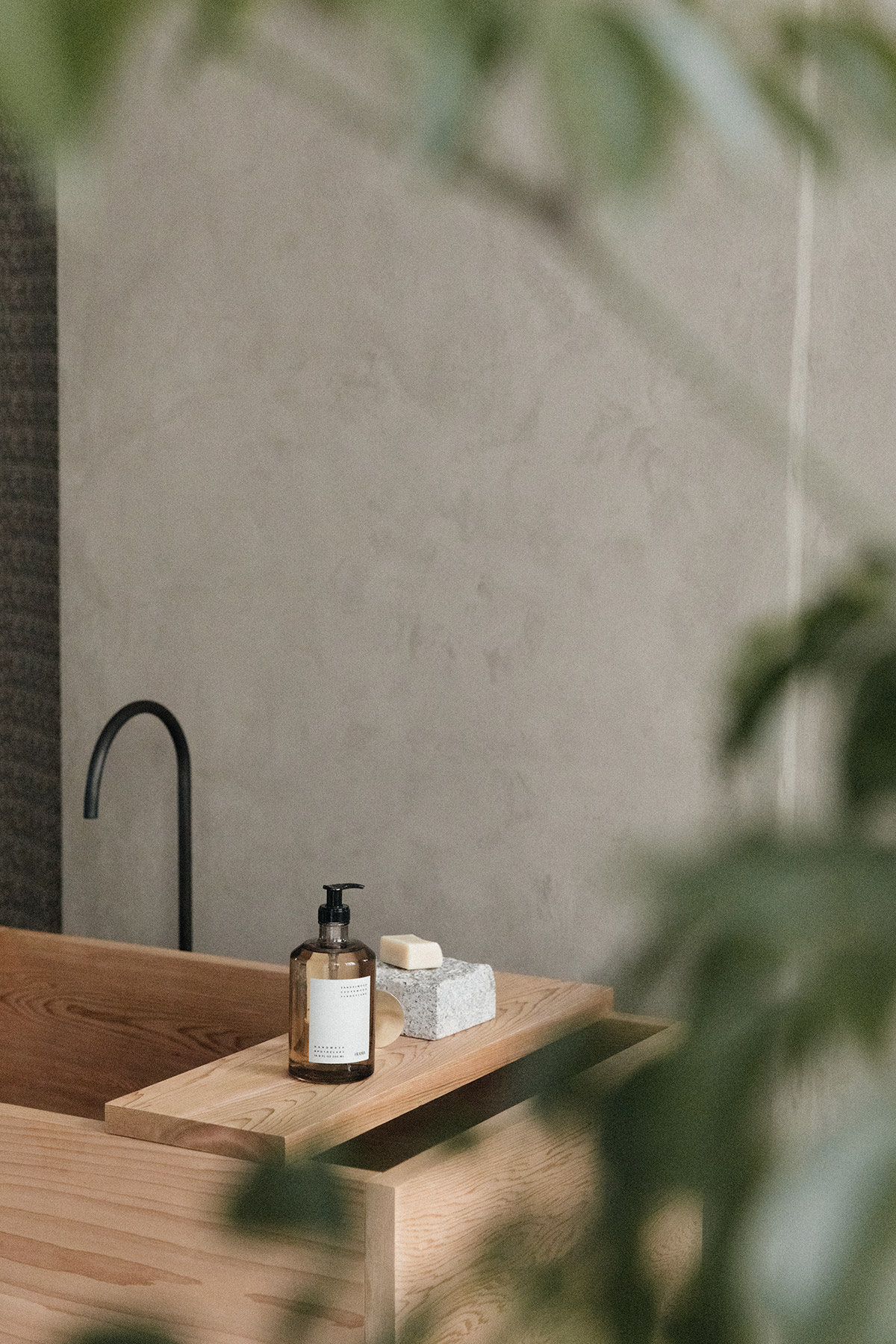 wooden bath tub against raw rendered wall surrounded by tranquil plants