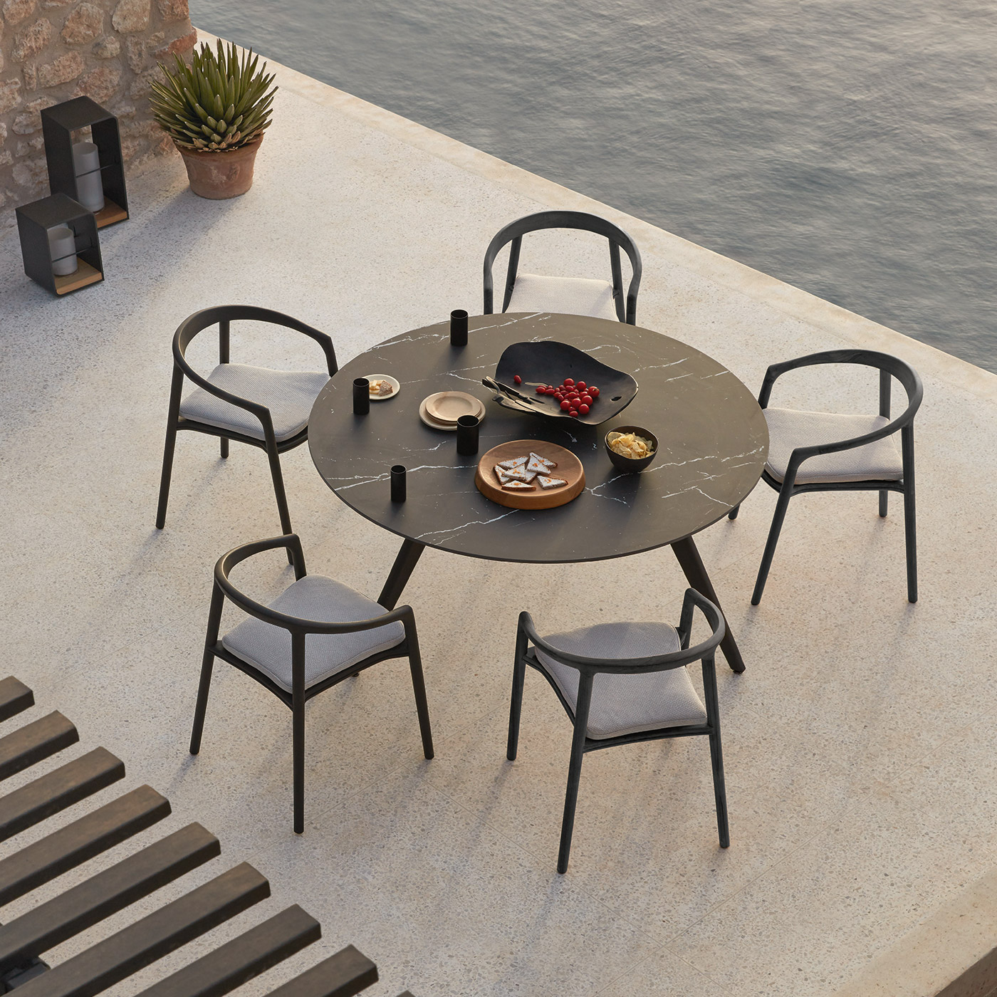 Torsa outdoor table in black ceramic with Solid outdoor armchairs in black teak next to water on Summer evening