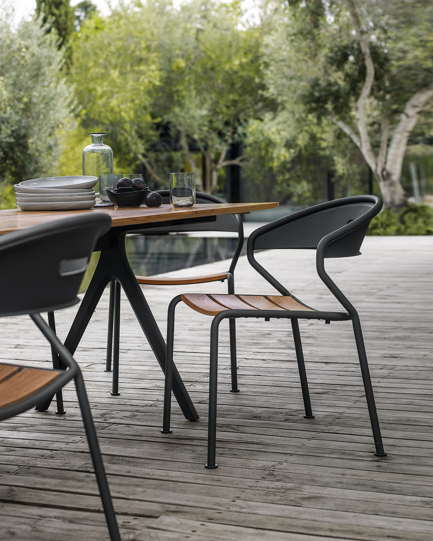 Dark grey aluminium and teak Curve chair by Gloster on modern wooden terrace with swimming pool and olive trees
