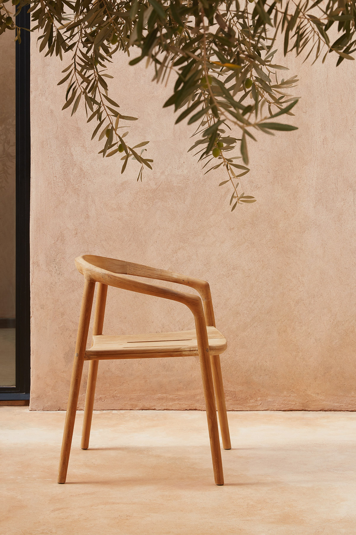 Solid outdoor armchair in teak by Manutti in modern mediterranean courtyard with olive tree