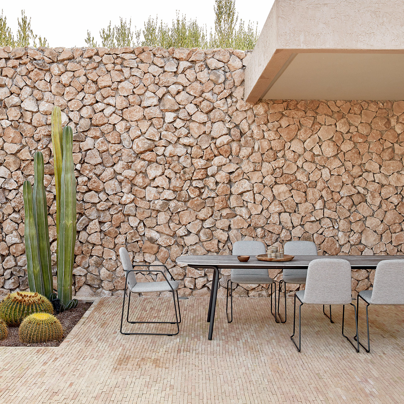 Outdoor loop chairs in black metal and grey fabric with outdoor dining table on rustic brick terrace with cacti