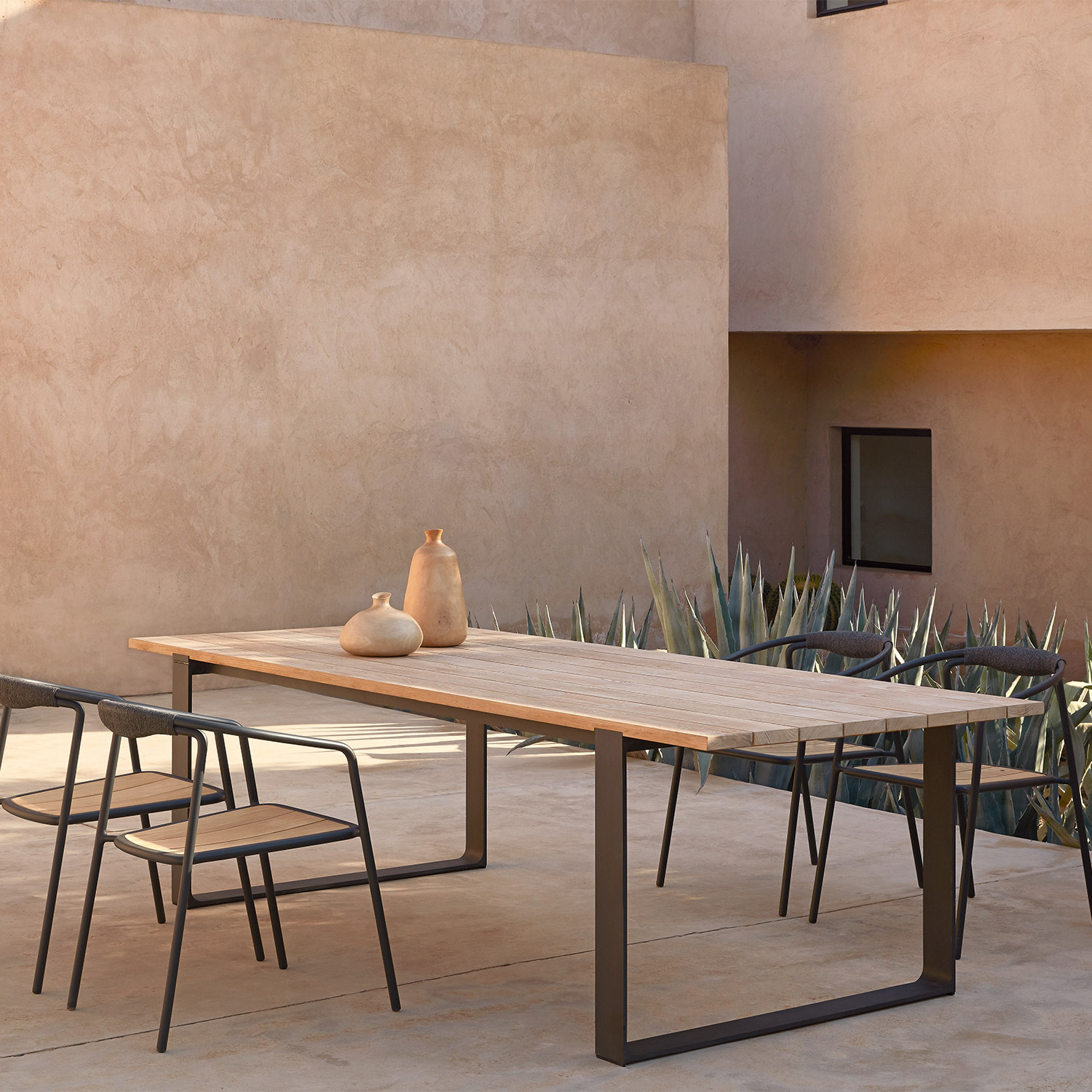 Modern teak and black metal outdoor dining table and chairs by Manutti next to modern Mediterranean house with aloe plants