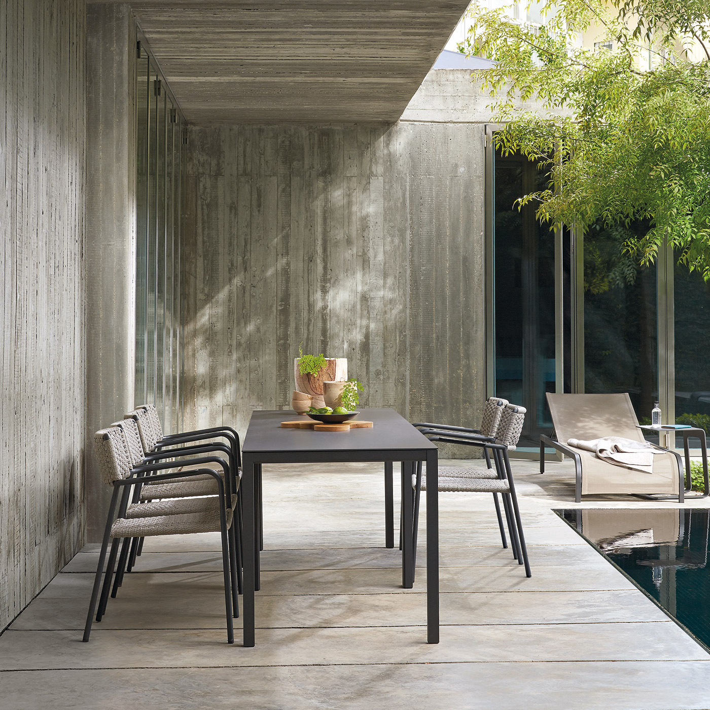 Outdoor metal Quarto table and chairs next to modern concrete house and swimming pool