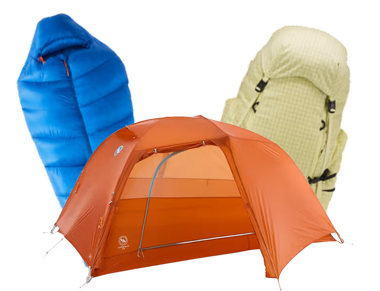 Orange dome tent with a blue sleeping bag and a light green backpack behind it, all outdoor camping gear.