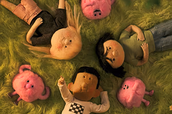 Three animated characters and three pink brains lying on green grass, looking upward towards the sky during sunset on a summer day.