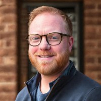 A picture of Christian outside his home, smiling wearing a shirt and glasses.