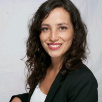 A headshot of Natalia Sanchez wearing a black suit against a grey background.