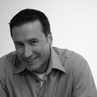 A gray-scale headshot of Todd laughing while wearing a dress shirt.