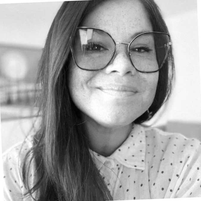A headshot of Laura smiling and wearing glasses and a collared shirt.