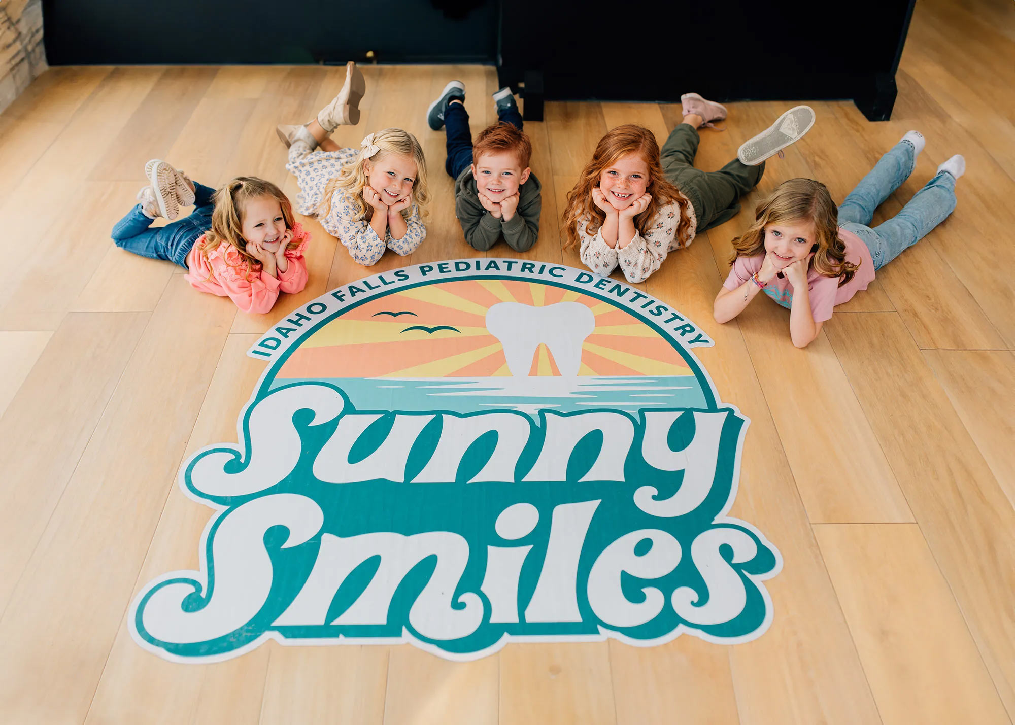 Group of kids laying on the floor of Sunny Smiles Logo
