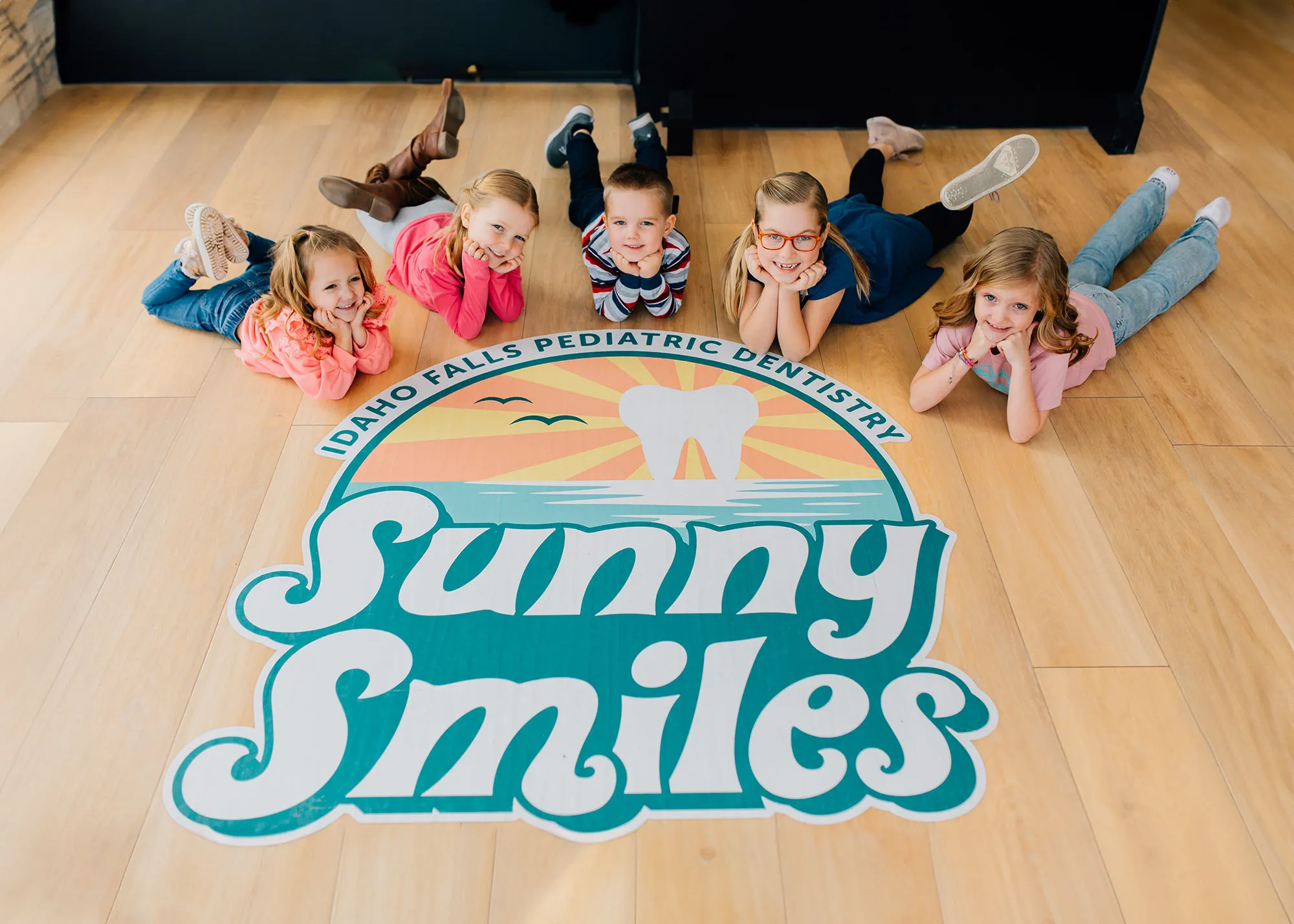 Group of kids laying on the floor of Sunny Smiles Logo