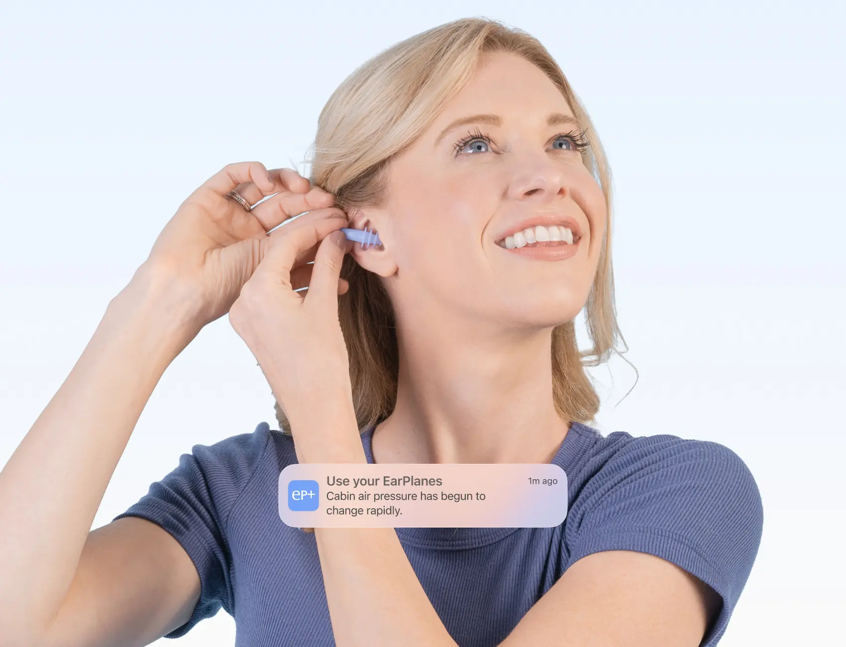 A woman smiling, inserting EarPlanes earplugs into her ear. At the bottom of the image is a phone notification from the EarPlanes+ app that notifies users when to use the product.