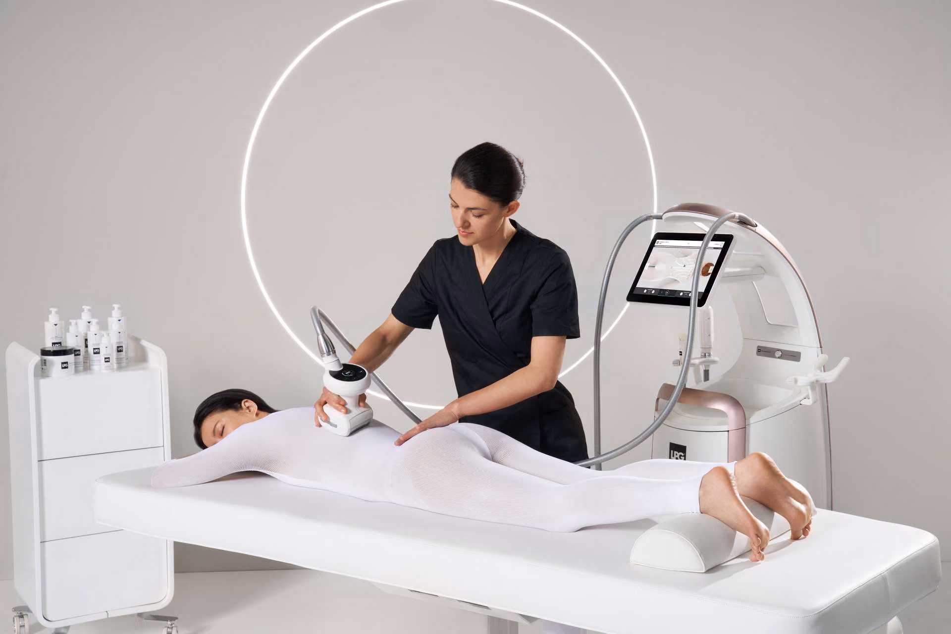 Woman in black uniform using a machine on a patient lying face down in white bodysuit for treatment.