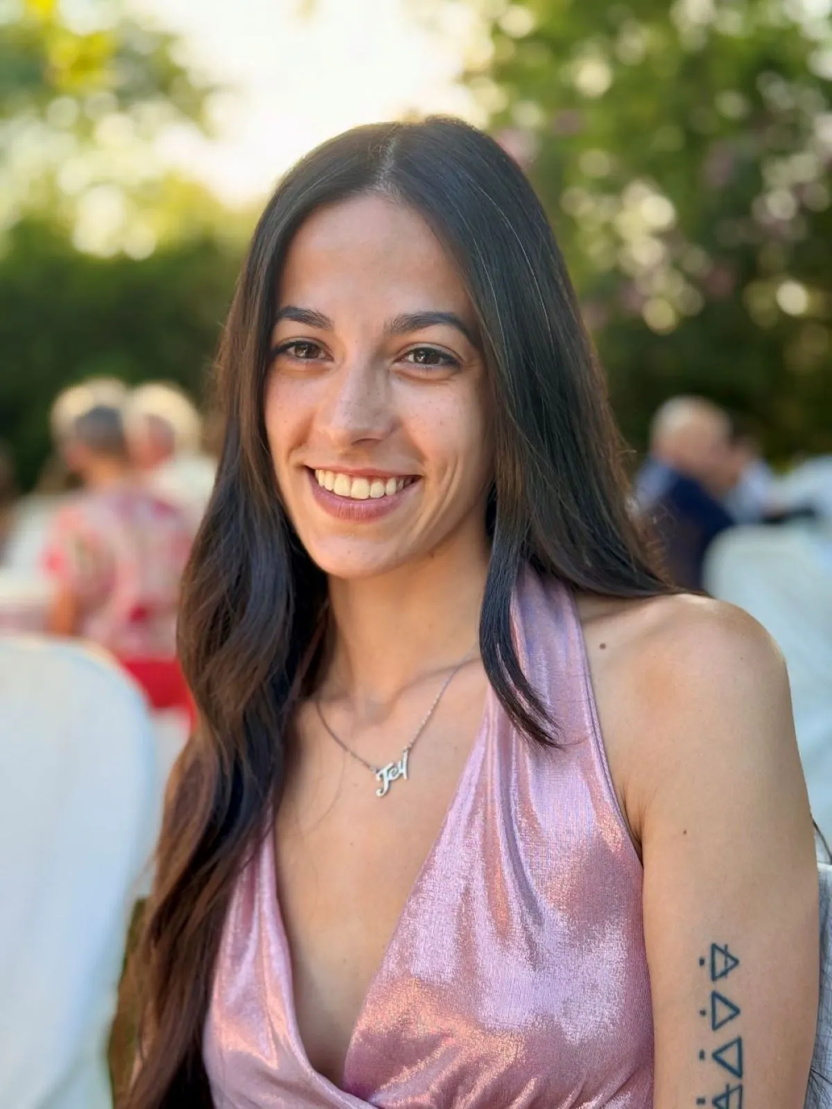 Jennifer Amadei sorridente durante un evento all'aperto, con abito rosa scintillante e atmosfera luminosa e serena