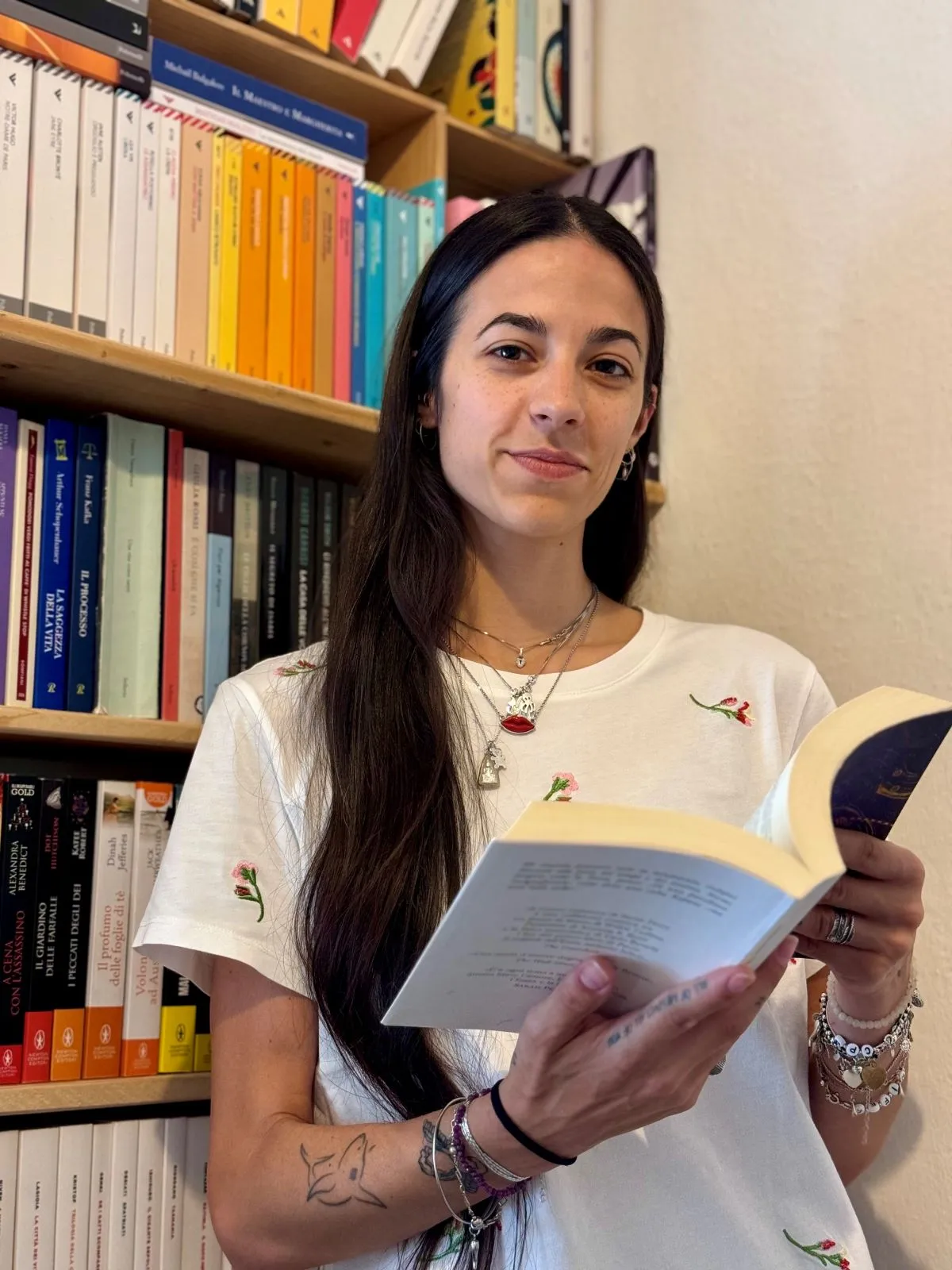Jennifer Amadei mentre legge un libro davanti a una libreria colorata, simbolo della sua passione per la lettura e la scrittura