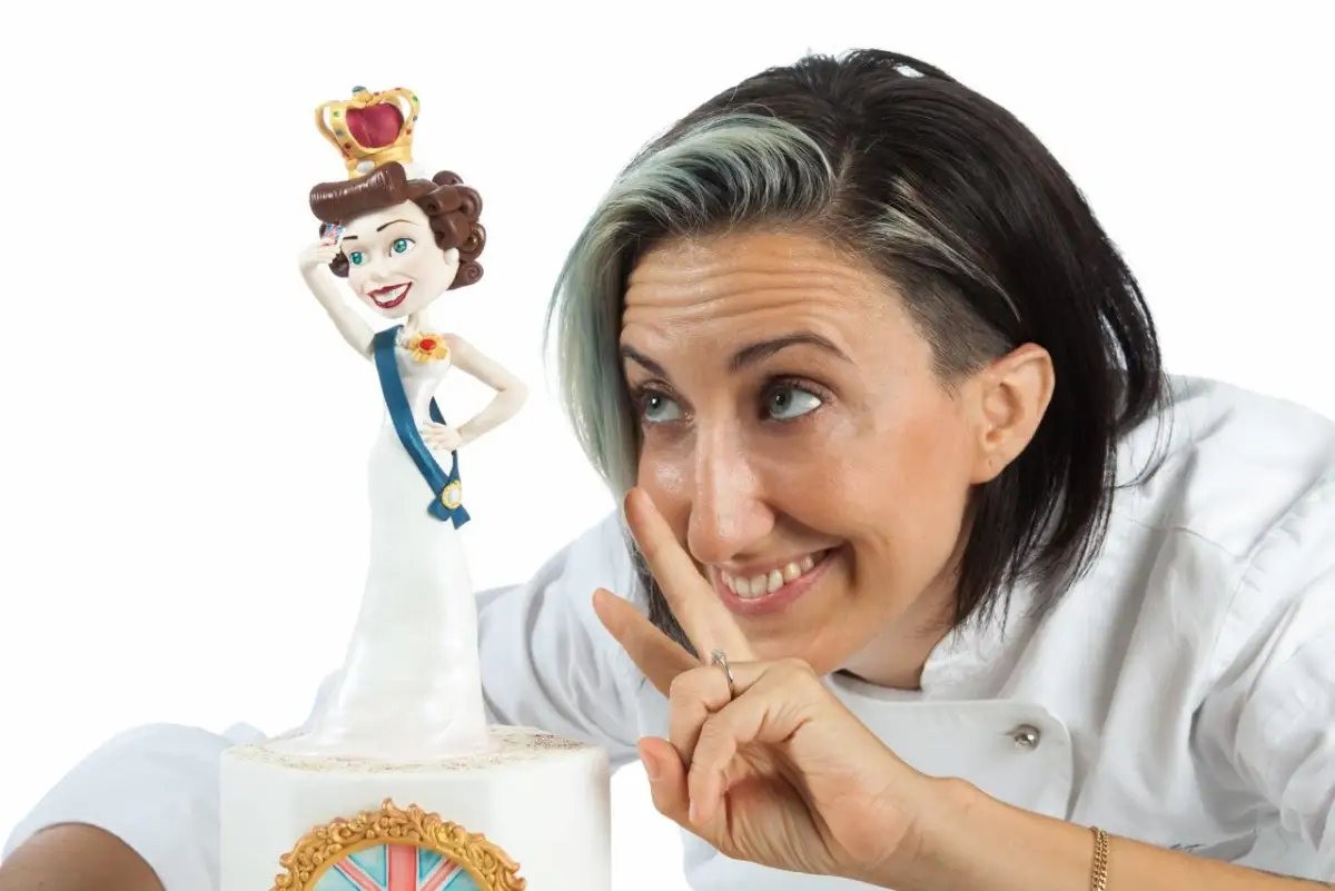 Silvia Mancini cake designer accanto a una torta scultura raffigurante la Regina Elisabetta con corona e sguardo ironico