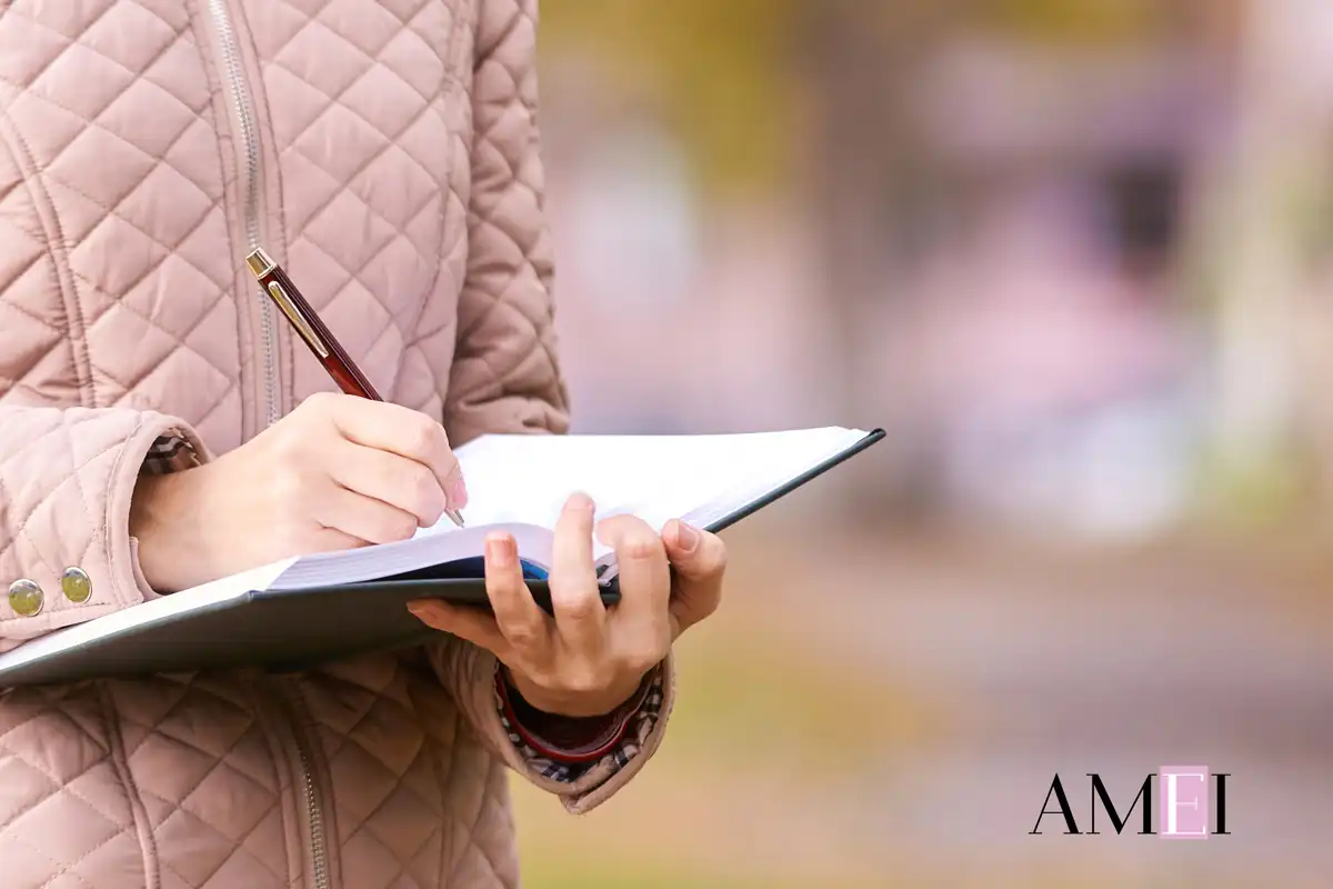 Donna con giacca trapuntata scrive su un quaderno all’aperto, in un contesto autunnale, firmato Amei Magazine