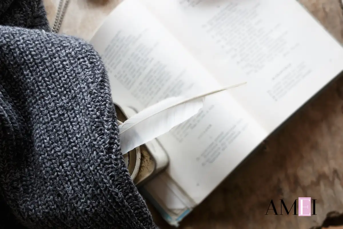 Piuma bianca su un libro aperto di poesie, avvolta in un maglione grigio, in uno stile caldo e intimo, firmato Amei Magazine
