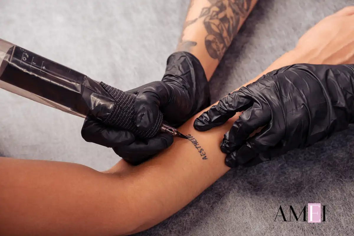 Tatuatore realizza un tatuaggio minimalista con la parola “Aesthetic” sul polso, indossando guanti neri
