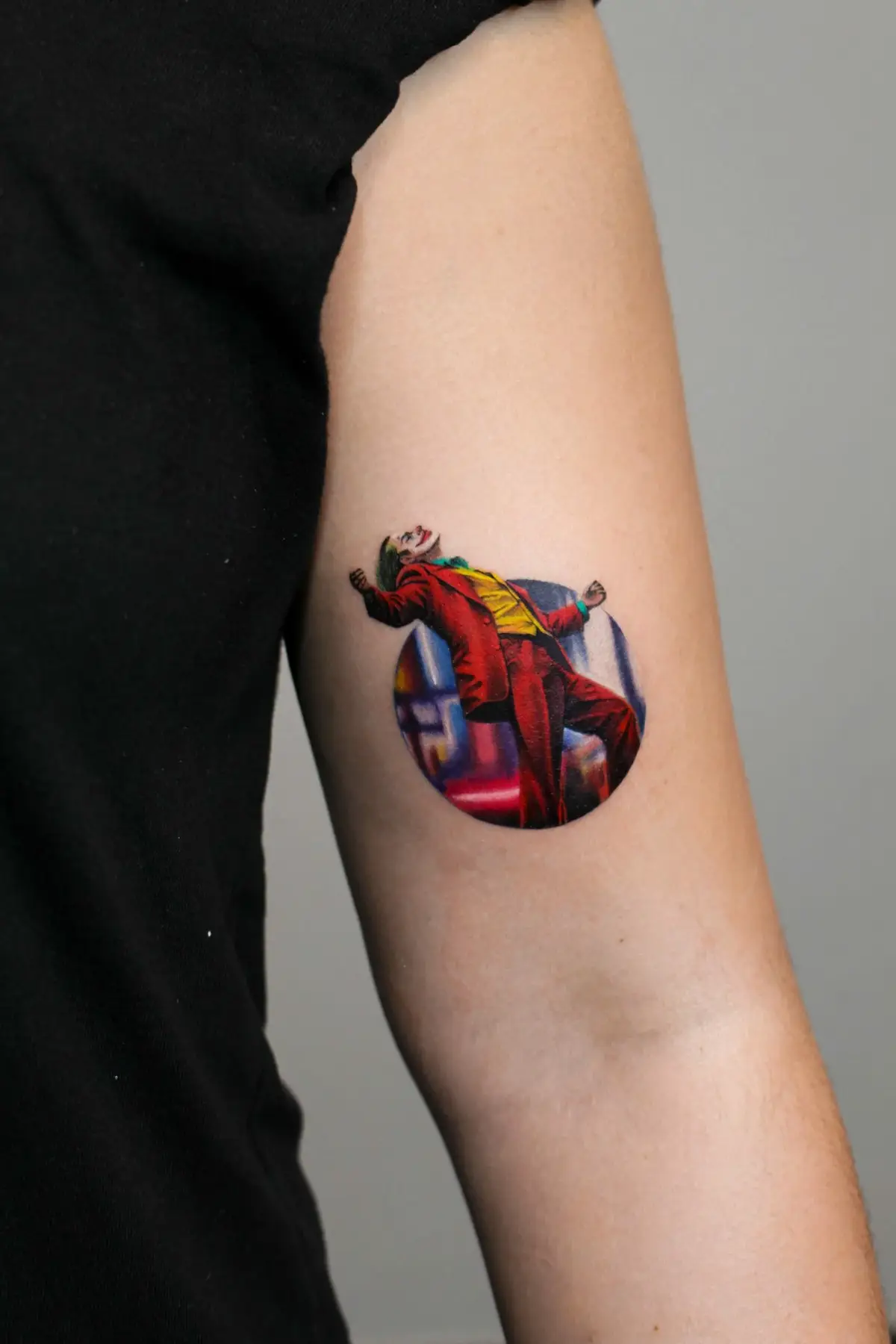 Tatuaggio microrealismo del Joker in posa iconica, colori vividi su braccio
