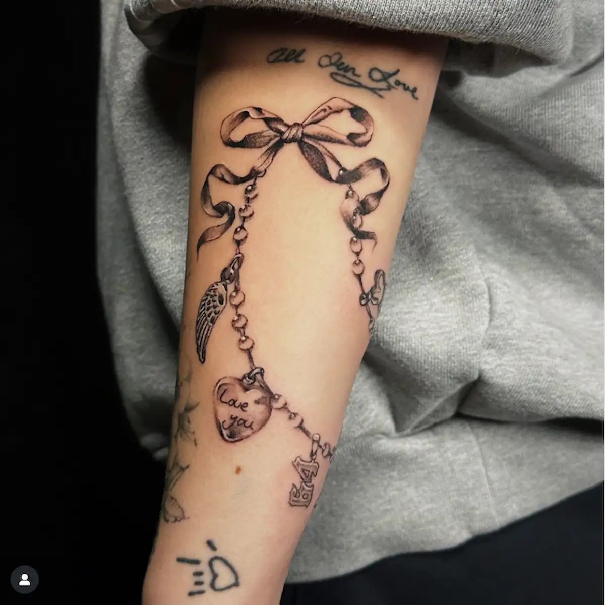 Tatuaggio a bracciale con fiocco e charm in inchiostro nero, dettagliati in stile fine line