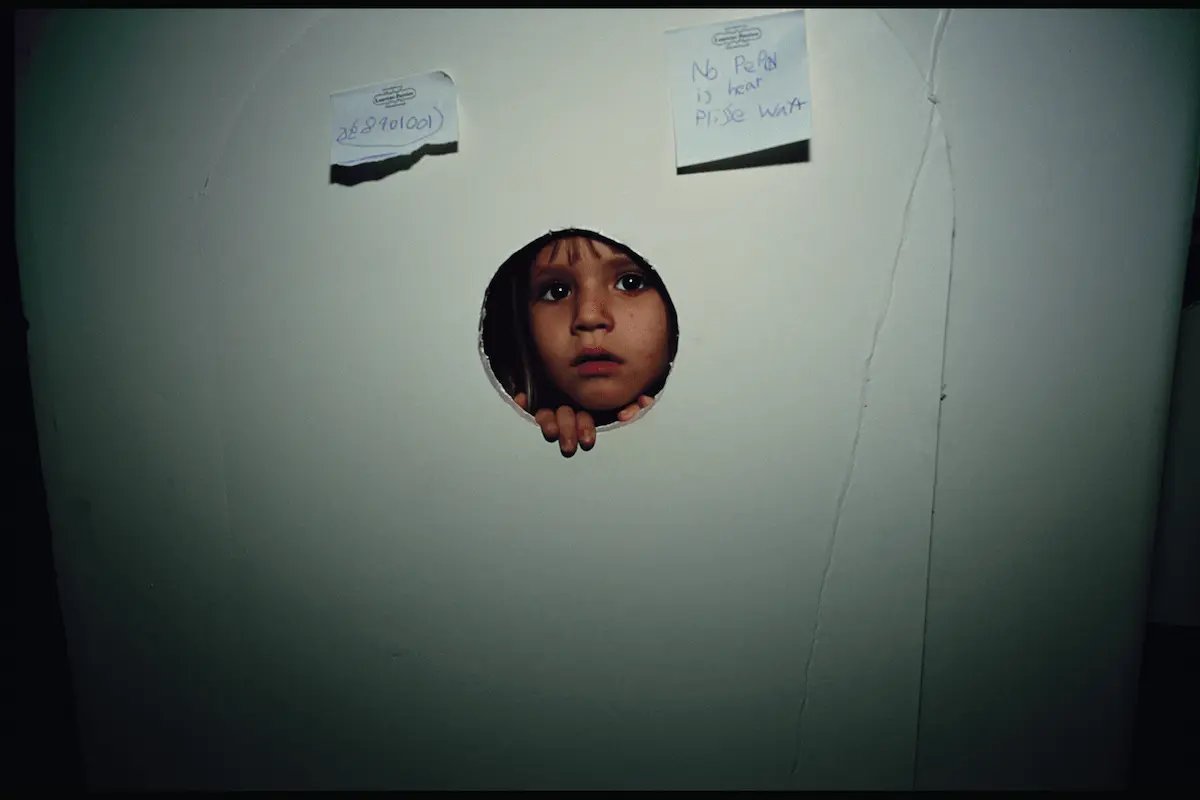 Ritratto di bambina che osserva da un foro nel pannello; fotografia di Nan Goldin in “This Will Not End Well”, Pirelli HangarBicocca