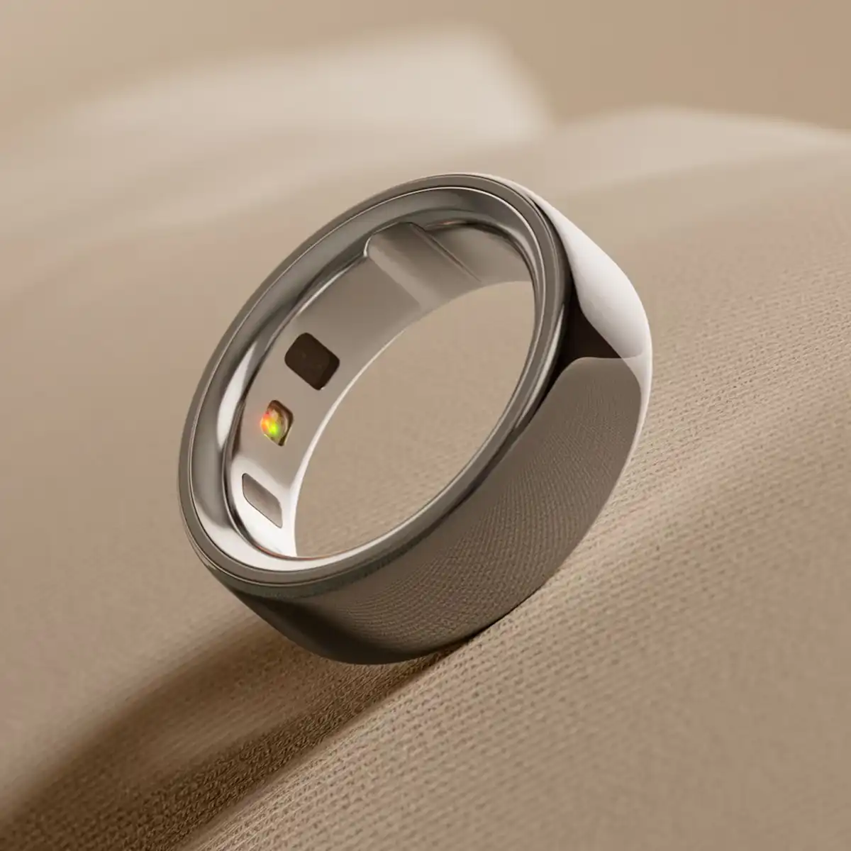Anello smart Oura Ring 4 in titanio su sfondo beige con sensori per sonno e benessere