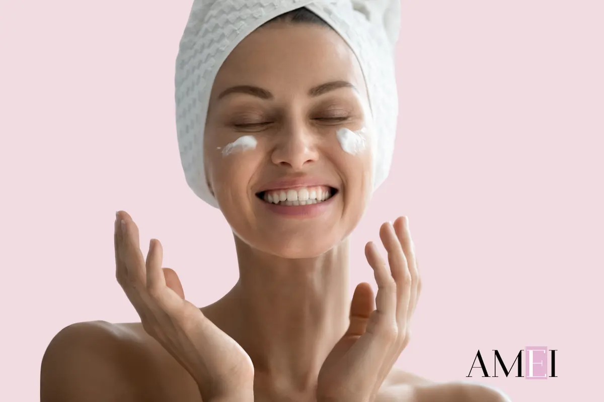 Donna sorridente con turbante applica crema idratante sul viso, routine skincare post vacanze per pelle luminosa.