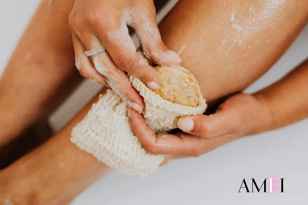 Mani femminili eseguono uno scrub corpo con spugna naturale e sapone, trattamento esfoliante post vacanze per pelle liscia.