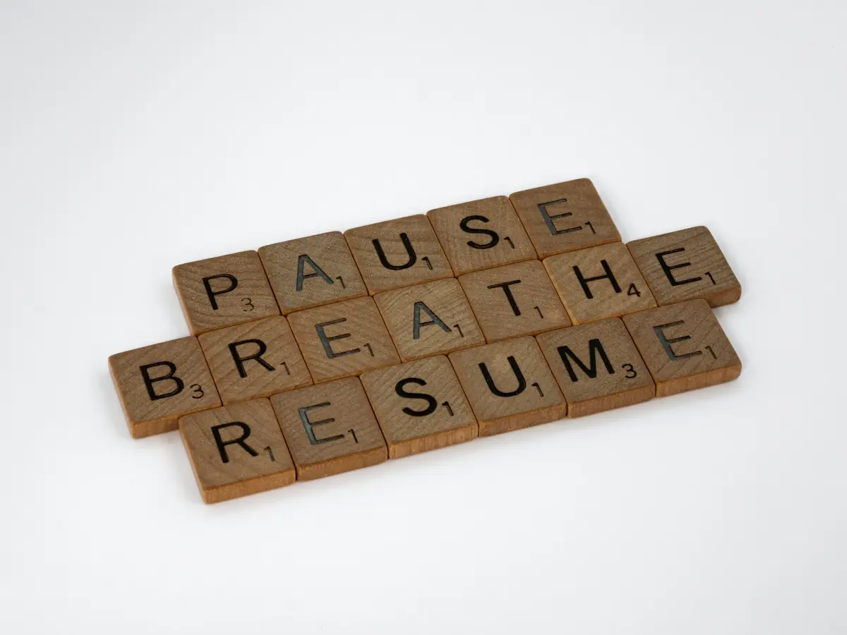 Scritta con tessere di legno “Pause, Breathe, Resume”, simbolo di mindfulness e pause consapevoli per ridurre lo stress.