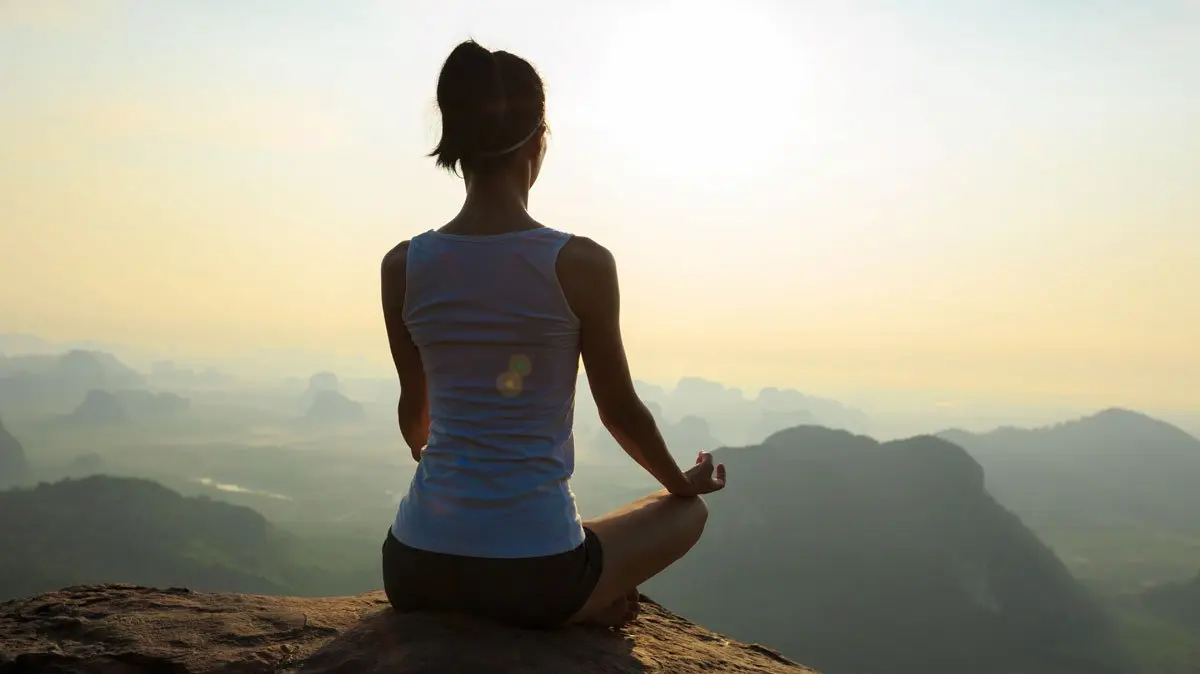 Donna in meditazione all’alba in montagna, simbolo di mindfulness e pause consapevoli per ridurre stress e ansia dopo le vacanze.