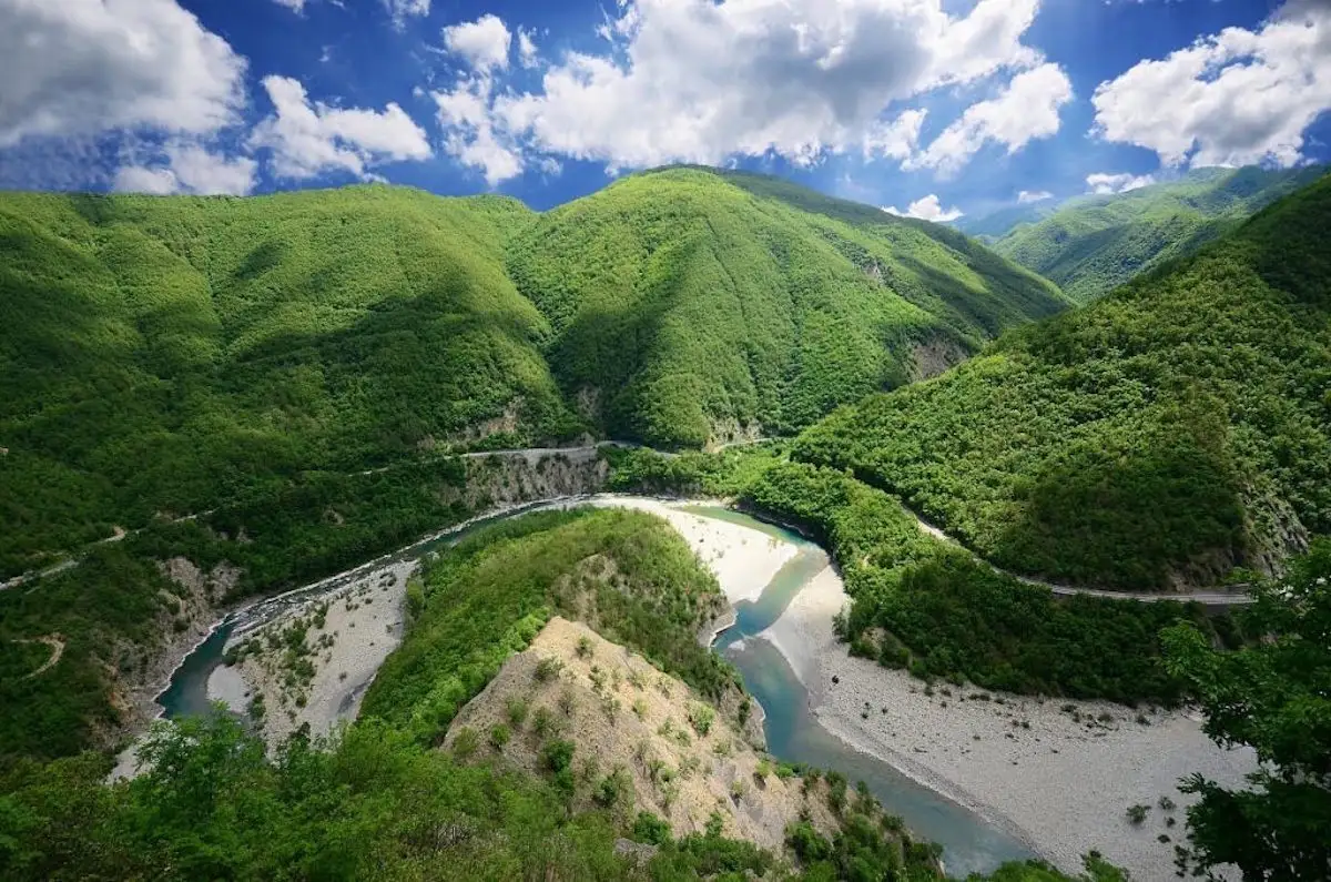 Veduta panoramica della Val Trebbia con il fiume che serpeggia tra verdi montagne e cielo azzurro.