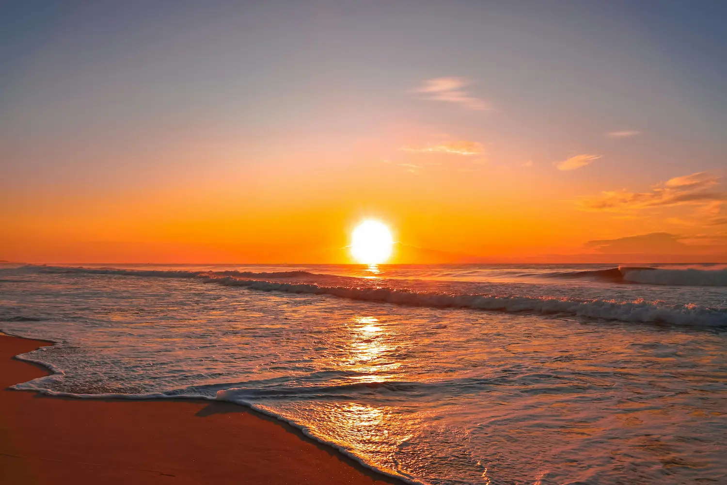 Tramonto sull’oceano con onde che si infrangono sulla sabbia, colori caldi che avvolgono cielo e acqua