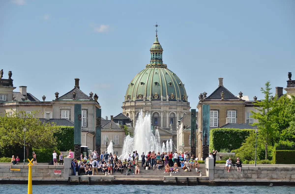 Veduta di Amalienborg e della Chiesa di Marmo a Copenaghen, con turisti sulla banchina e fontana centrale.